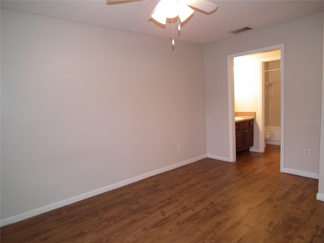 unfurnished bedroom featuring ensuite bath, dark wood-type flooring, and ceiling fan