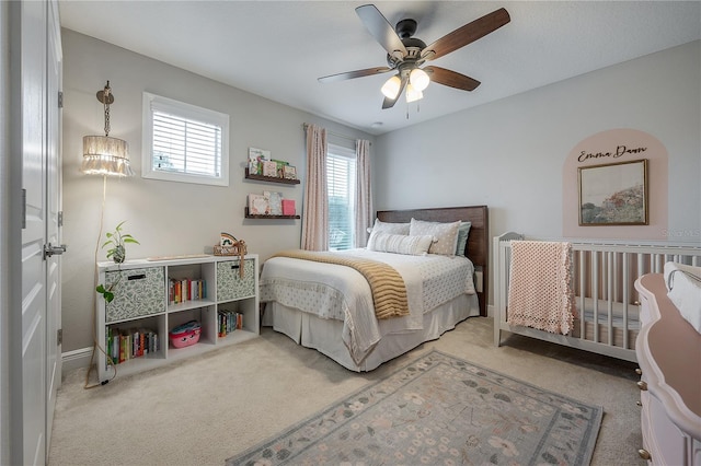 carpeted bedroom with ceiling fan and a nursery area