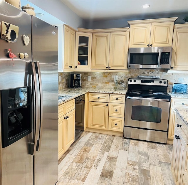 kitchen with light wood-type flooring, light stone counters, appliances with stainless steel finishes, and tasteful backsplash