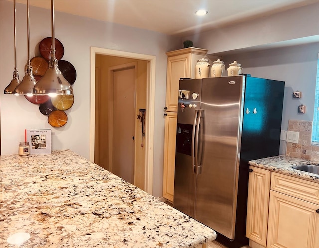 kitchen featuring stainless steel refrigerator with ice dispenser, pendant lighting, cream cabinetry, light stone countertops, and decorative backsplash