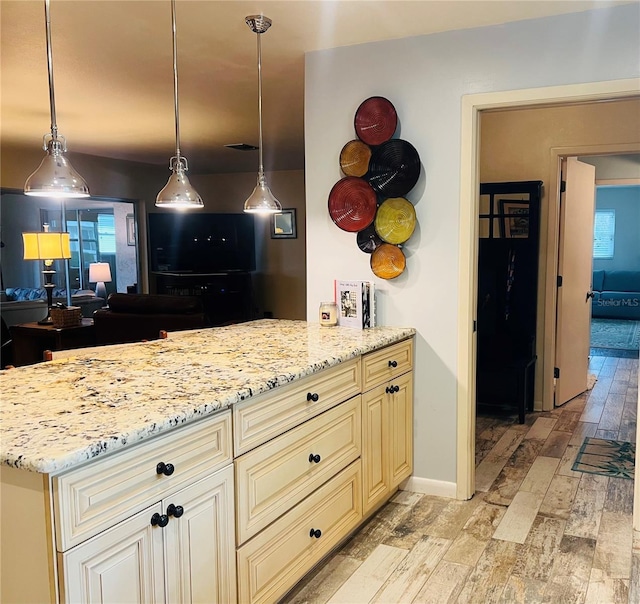 kitchen featuring decorative light fixtures, light stone counters, light hardwood / wood-style flooring, and cream cabinets