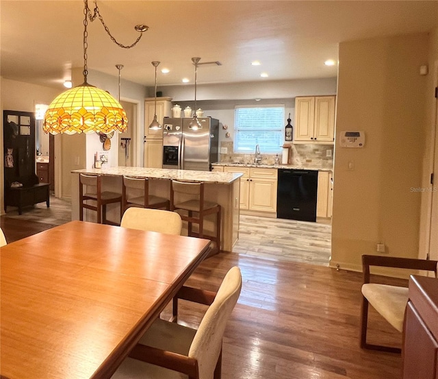 kitchen featuring a center island, black dishwasher, light stone countertops, stainless steel refrigerator with ice dispenser, and decorative light fixtures