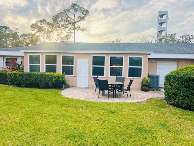 back house at dusk with a garage, central air condition unit, a yard, and a patio