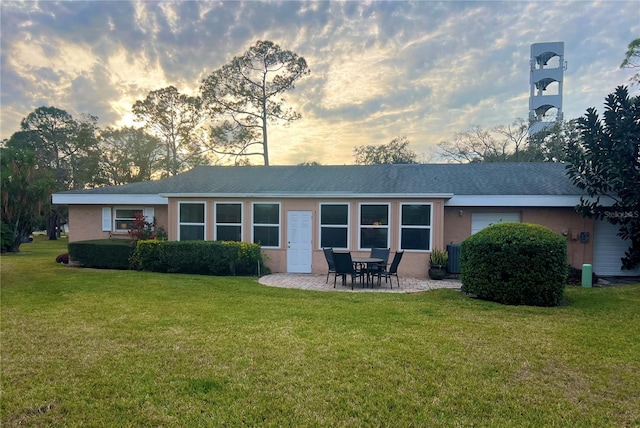 back house at dusk featuring a lawn and a patio