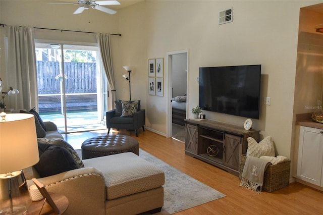 living room with light hardwood / wood-style floors, ceiling fan, and a high ceiling