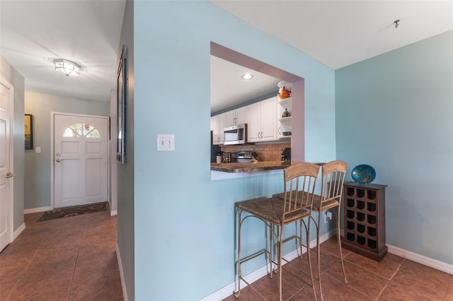 kitchen featuring dark tile patterned flooring, white cabinets, backsplash, kitchen peninsula, and a breakfast bar