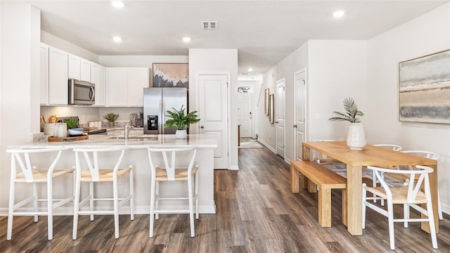 kitchen with sink, appliances with stainless steel finishes, dark hardwood / wood-style floors, white cabinets, and a kitchen bar