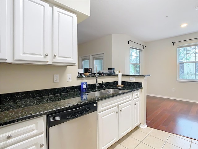 kitchen with light tile patterned floors, stainless steel dishwasher, sink, white cabinets, and dark stone counters