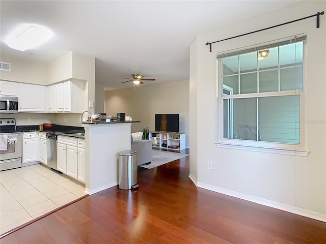 kitchen with kitchen peninsula, ceiling fan, sink, white cabinets, and stainless steel appliances