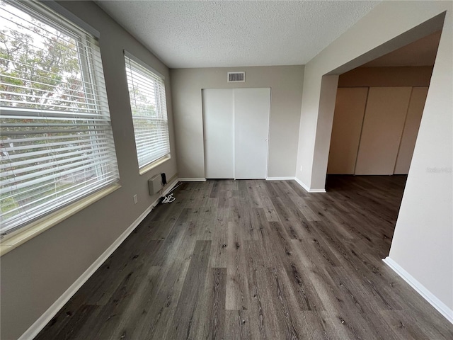 unfurnished bedroom with a wall mounted AC, dark wood-type flooring, a textured ceiling, and a closet