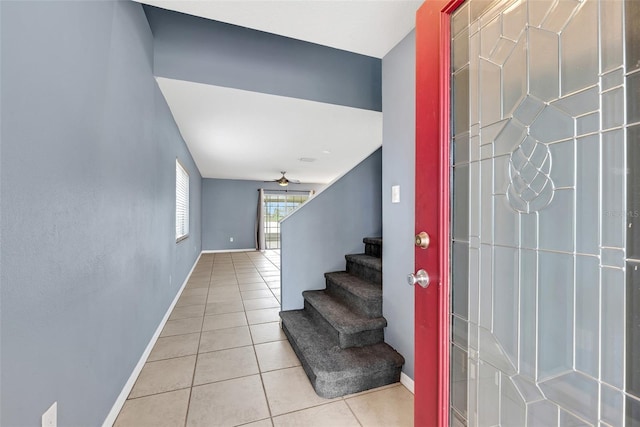 tiled entryway featuring baseboards, a ceiling fan, and stairs