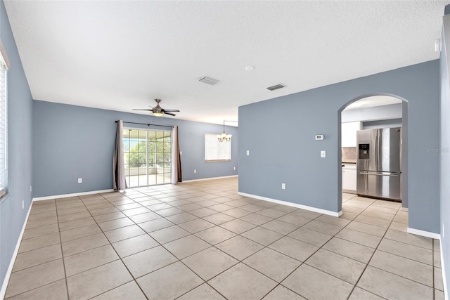 empty room featuring visible vents, baseboards, light tile patterned floors, ceiling fan with notable chandelier, and arched walkways