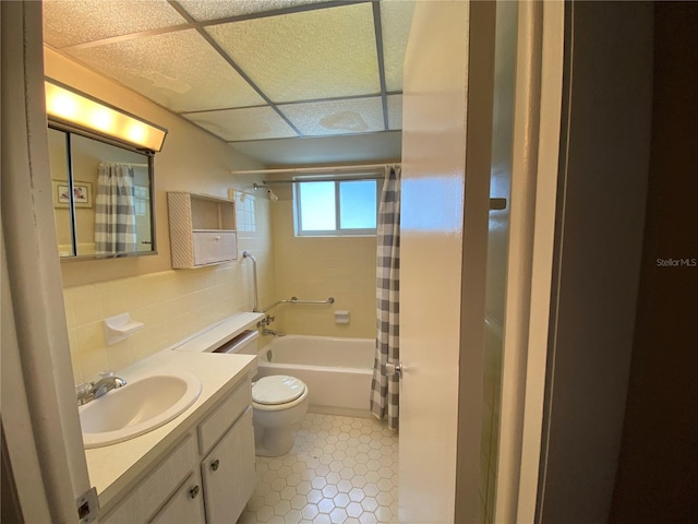 full bathroom with a paneled ceiling, tile patterned floors, vanity, shower / bath combination with curtain, and toilet