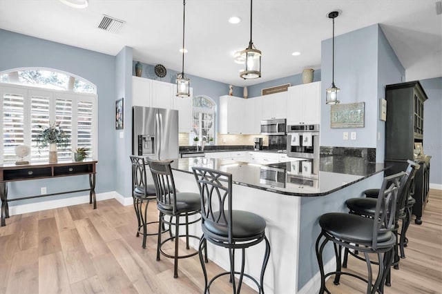 kitchen with white cabinetry, decorative light fixtures, stainless steel appliances, and light wood-type flooring