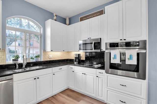 kitchen featuring sink, white cabinetry, stainless steel appliances, dark stone counters, and light wood-type flooring