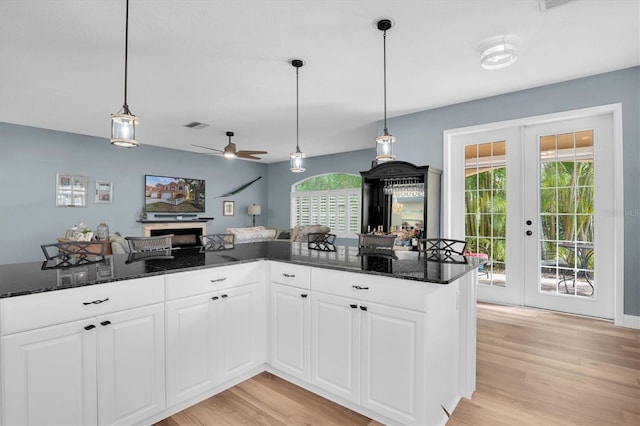 kitchen with pendant lighting, dark stone countertops, white cabinets, french doors, and light wood-type flooring