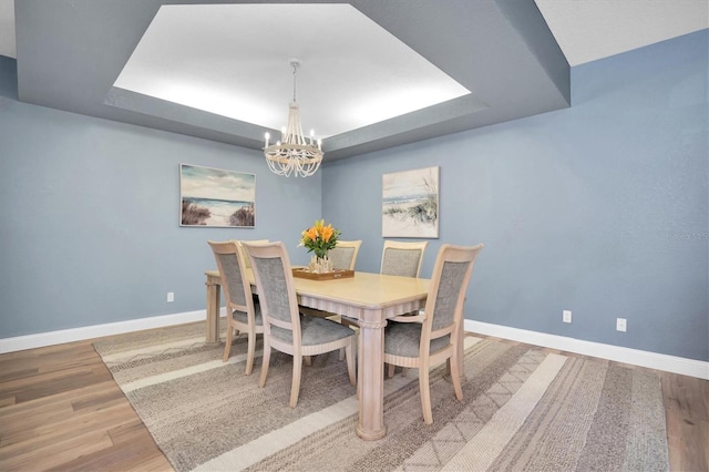 dining space featuring a raised ceiling, hardwood / wood-style floors, and an inviting chandelier