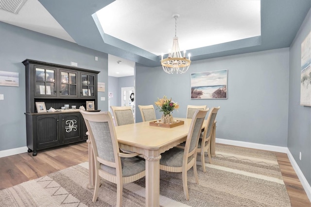 dining space with a raised ceiling, an inviting chandelier, and light wood-type flooring