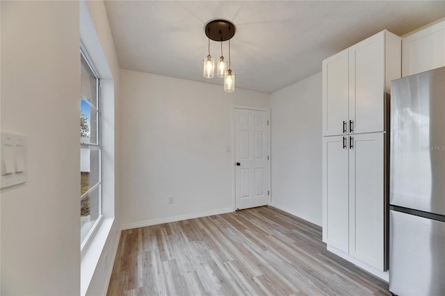 unfurnished dining area featuring a textured ceiling and light wood-type flooring