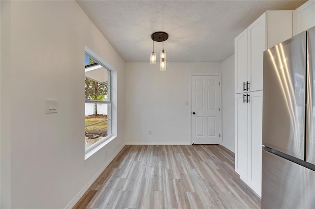 unfurnished dining area with a wealth of natural light, light hardwood / wood-style flooring, and a textured ceiling