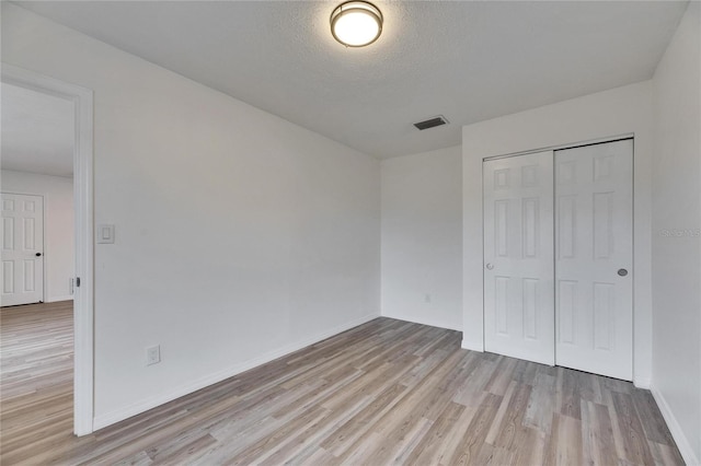 unfurnished bedroom with a closet, light wood-type flooring, and a textured ceiling