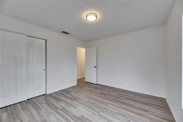 unfurnished bedroom featuring a textured ceiling, a closet, and light wood-type flooring