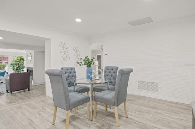 dining area featuring brick wall, ornamental molding, and light hardwood / wood-style flooring