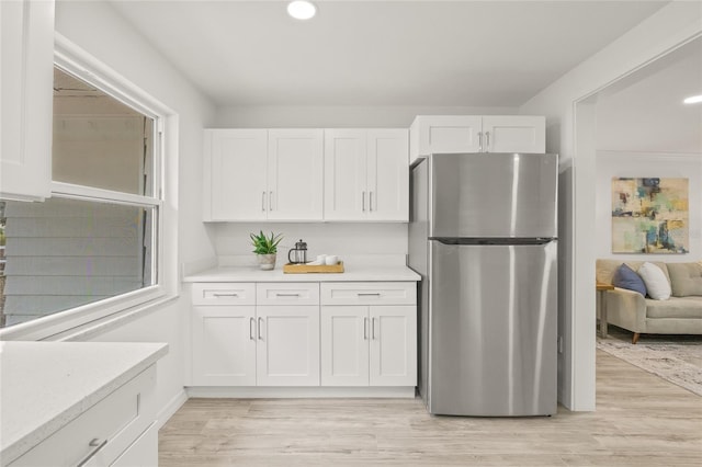 kitchen with light stone counters, stainless steel fridge, light wood-type flooring, and white cabinets