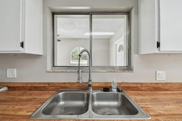 interior details with white cabinetry, sink, and wooden counters