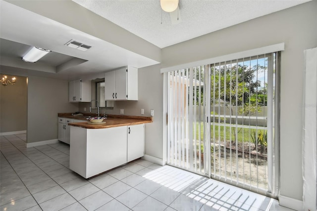 kitchen with light tile patterned flooring, wood counters, sink, white cabinets, and a textured ceiling