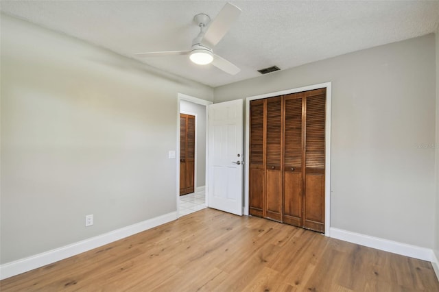 unfurnished bedroom featuring ceiling fan, a textured ceiling, light hardwood / wood-style floors, and a closet