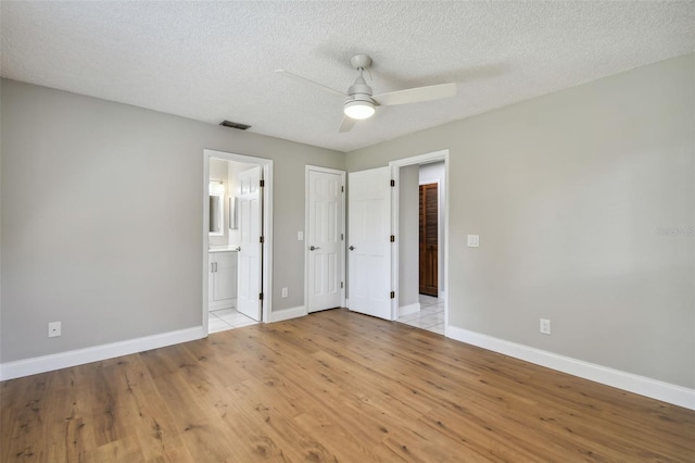 unfurnished bedroom featuring ceiling fan, ensuite bath, a textured ceiling, and light wood-type flooring