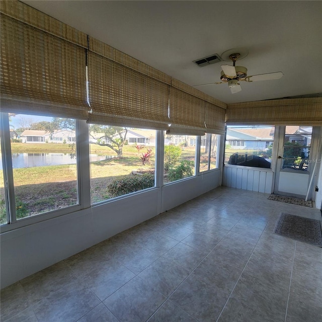 unfurnished sunroom with a ceiling fan, a water view, and visible vents