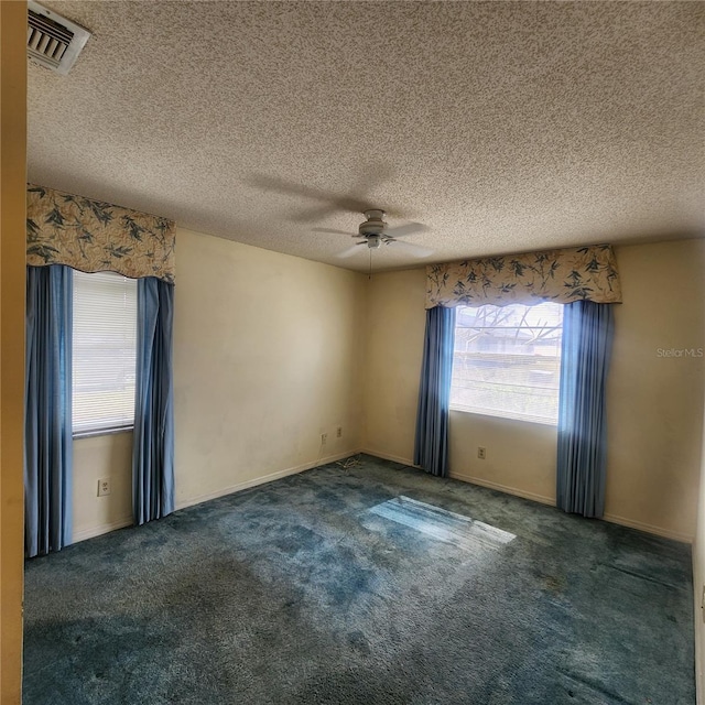 unfurnished room with dark colored carpet, a healthy amount of sunlight, and visible vents