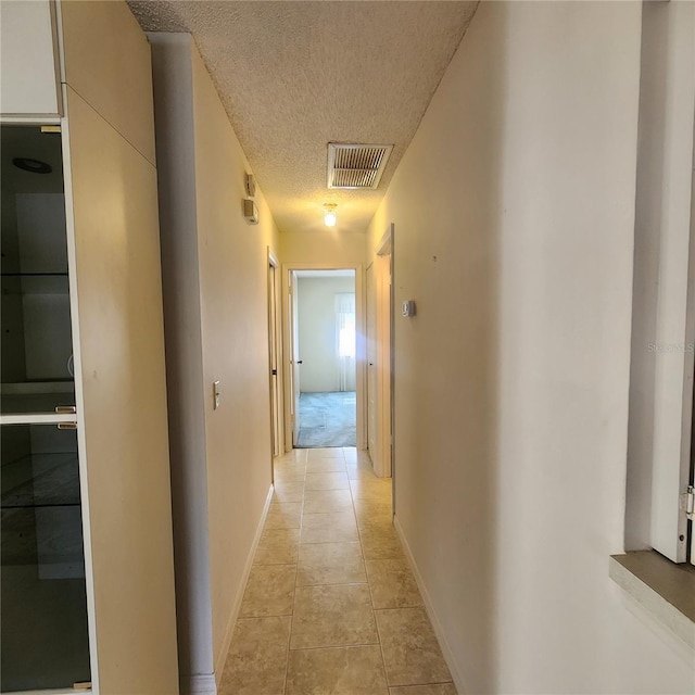 hallway with light tile patterned floors, baseboards, visible vents, and a textured ceiling