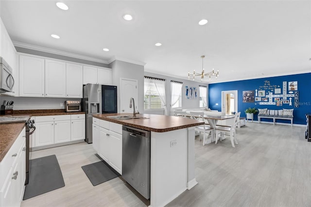 kitchen with white cabinetry, stainless steel appliances, decorative light fixtures, and a kitchen island with sink