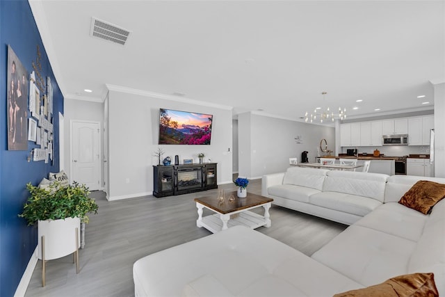 living room with ornamental molding, a notable chandelier, and light hardwood / wood-style flooring