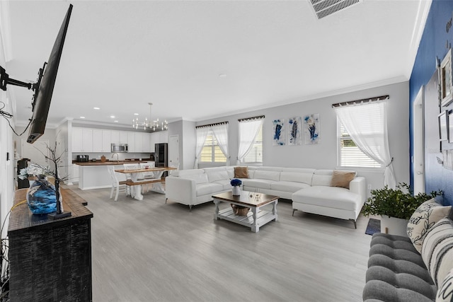 living room with ornamental molding, an inviting chandelier, and light hardwood / wood-style flooring