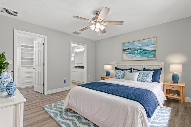 bedroom with ensuite bathroom, a textured ceiling, a walk in closet, light wood-type flooring, and ceiling fan