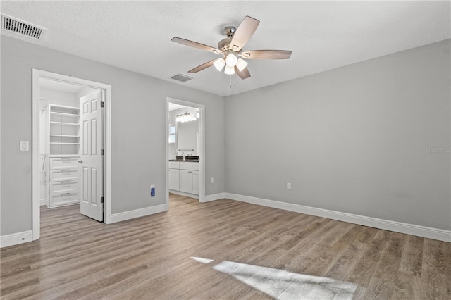 unfurnished bedroom with a spacious closet, light hardwood / wood-style floors, a closet, ceiling fan, and ensuite bathroom