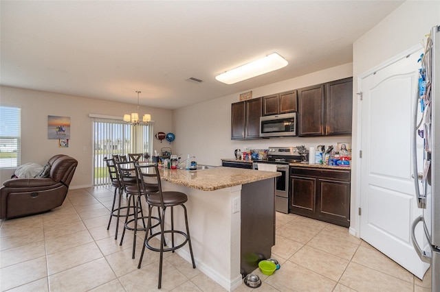 kitchen featuring a breakfast bar, dark brown cabinetry, decorative light fixtures, an island with sink, and stainless steel appliances