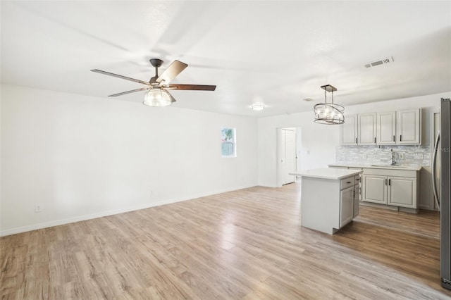 kitchen with gray cabinets, a kitchen island, pendant lighting, decorative backsplash, and light hardwood / wood-style floors