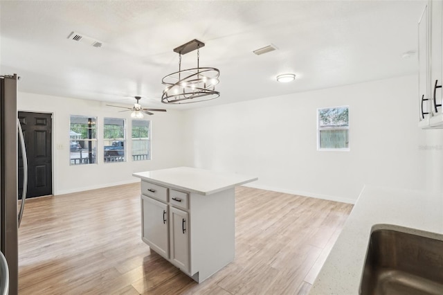 kitchen with light hardwood / wood-style flooring, stainless steel fridge, hanging light fixtures, plenty of natural light, and white cabinets