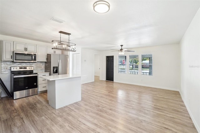 kitchen with a kitchen island, appliances with stainless steel finishes, gray cabinetry, decorative backsplash, and hanging light fixtures