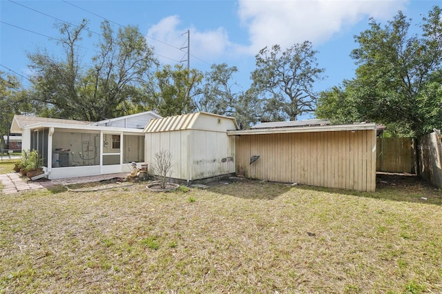 back of property featuring a sunroom, a yard, and a storage unit