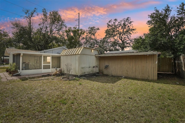 back house at dusk with a shed, a lawn, and a sunroom