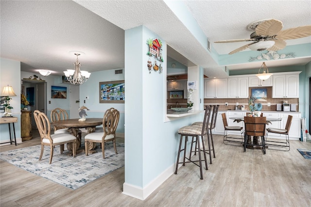 kitchen featuring light hardwood / wood-style floors, a textured ceiling, white cabinets, backsplash, and a breakfast bar area