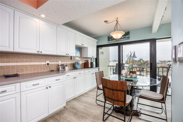 kitchen with pendant lighting, white cabinets, a textured ceiling, decorative backsplash, and beam ceiling