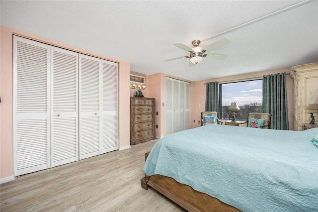 bedroom with multiple closets, ceiling fan, light hardwood / wood-style flooring, and a textured ceiling