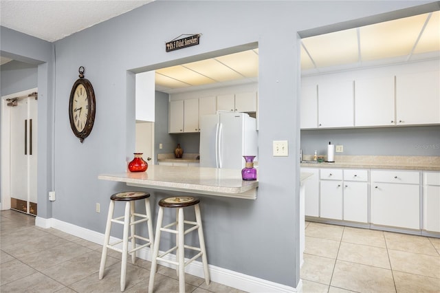 kitchen featuring a breakfast bar area, white cabinetry, light tile patterned floors, and white fridge